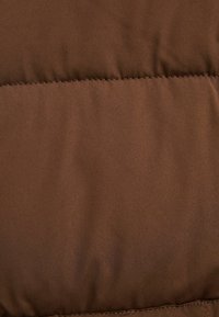 Brun väv med en mjuk textur, som har en kviltad design. Ytan har en lätt glans och synliga sömmar längs kanterna.