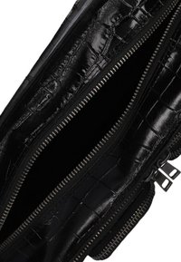 Zwarte krokodillen-embossed leren tas met een interieur dat bestaat uit dubbele ritscompartimenten en een gladde, glanzende textuur. Het interieur is gevoerd met zwarte stof.