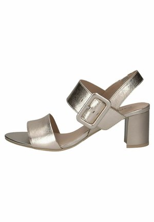 Metallic gold heeled sandals with a wide toe strap, an ankle strap featuring a square buckle, and a block heel. Smooth texture and modern design.