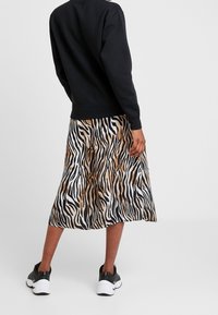 Sweatshirt noir, jupe mi-longue avec un motif rayé tigre en noir, blanc et beige, accompagnée de baskets athlétiques noires.