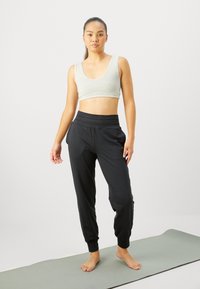 Pelēks saīsināts tops un melni sporta bikses, kas izgatavotas no mīkstas auduma, ar elastīgu jostu un sašaurinātiem potītes daļām, novietoti uz jogas paklāja.