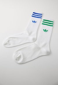 Bela delovna nogavica z rebrasto teksturo, z modrimi in zelenimi črtami na vrhu ter vezenim logotipom Adidas v usklajenih barvah.