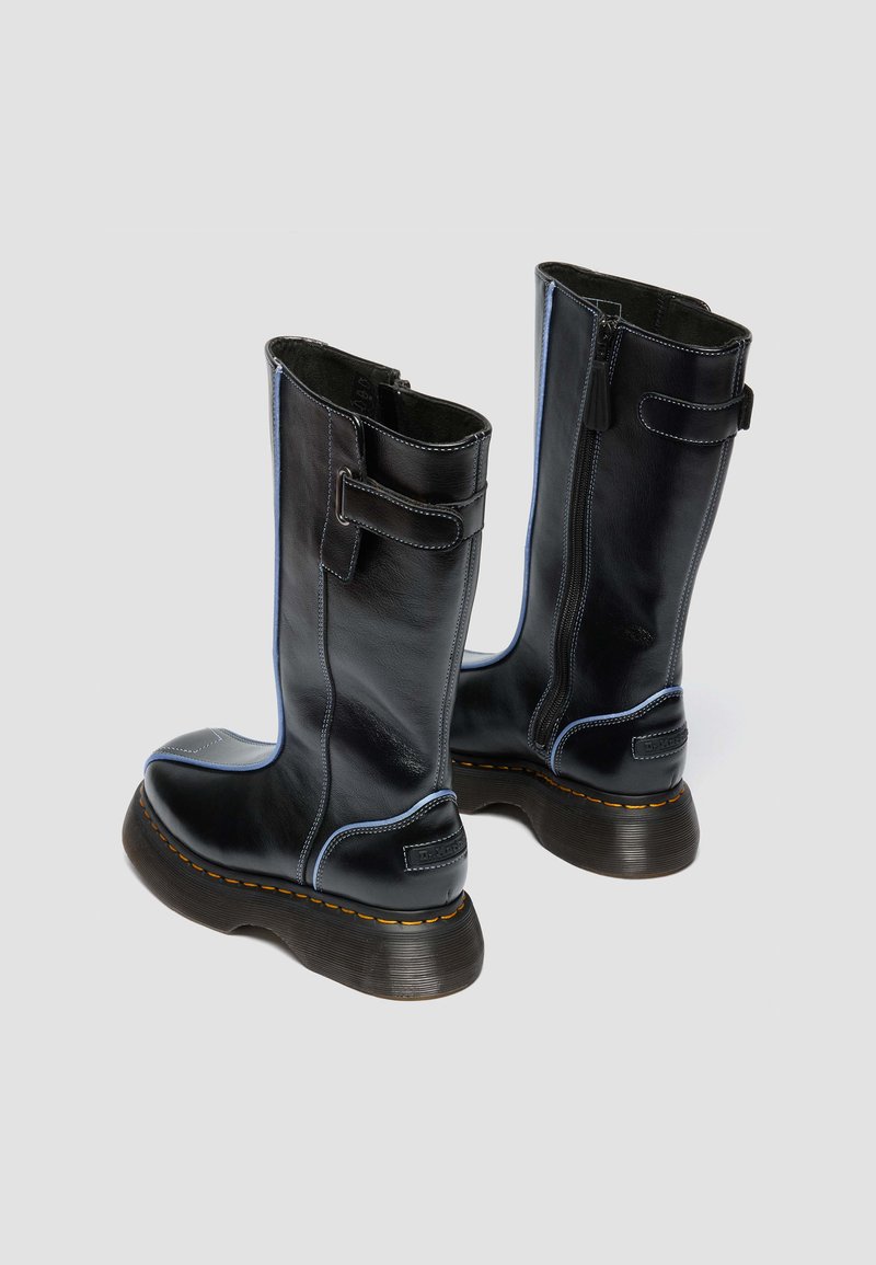 Black leather mid-calf boots with side zippers, adjustable straps, thick textured soles, and light blue stitching detail.