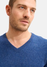V-Ausschnitt Pullover in einem tiefen Blauton, aus weichem Stoff mit glatter Textur; verfügt über einen klassischen gerippten Kragen und minimale Nähte.
