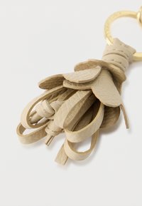 Accessorio portachiavi in pelle beige con forme di foglie sovrapposte, finitura texturizzata e un anello in metallo dorato per il fissaggio.