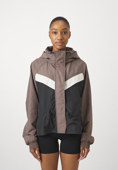 Braun und schwarze Windbreaker-Jacke mit color-blocked Design und einem weißen Chevron-Muster, verstellbare Kapuze und Kordelzug in der Taille.