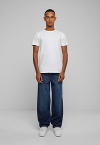 Hvid kortærmet t-shirt kombineret med løse blå denim jeans og hvide sneakers, med et enkelt og lige design.