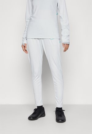 Lichtgrijze sportset bevat een langslavige top met contrasterende turquoise accenten en slim-fit broek. De stof lijkt glad en flexibel.