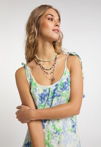 Ärmelloses Kleid im blau-grünen Batikmuster mit schwachen floralen Akzenten. Verfügt über verstellbare Schulterbänder und geschichtete Perlenketten.