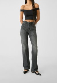 Musta off-the-shoulder -paita yhdistetty korkeavyötäröisiin, suoralahkeisiin harmaisiin farkkuihin. Farkuissa on haalistunut pinta ja vähäiset yksityiskohdat.