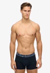 Boxer briefs navy con una cintura elastica grigia che presenta il logo "SUPERDRY". Realizzati in materiale morbido, design aderente con cuciture minime.