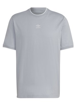 Osoba ubrana w jasnoszary t-shirt, niebieskie podwinięte jeansy, białe trampki, biały sweter zawiązany w pasie oraz czarna torba na ramię.