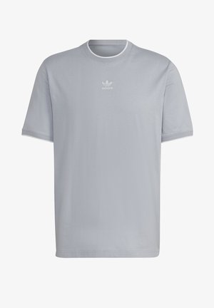 Persoon draagt lichtgrijze t-shirt, blauwe opgerolde spijkerbroek, witte sneakers, wit sweatshirt om de taille geknoopt en een zwarte crossbody tas.