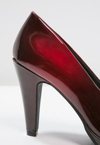 Pompe à talons aiguilles en cuir verni rouge avec un bout fermé, au design épuré et d'un talon stiletto. Texture lisse avec une finition brillante.