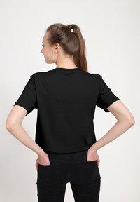 Sort t-shirt med korte ærmer og rund udskæring, lavet af glat stof, vist fra ryggen, parret med mørke denimjeans.