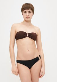 Brūns metalizēts bandeau bikini tops ar priekšējo savilkumu un zelta akcentu, kombinēts ar melniem zemu jostasvīru bikini apakšiem ar sānu savilkumu.