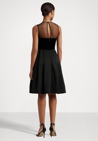 Svart klänning med en åtsittande bodice i sammet, genomskinlig meshrygg och veckad kjol. Bärs med svarta högklackade sandaler.