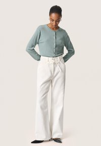 Cardigan verde chiaro a coste con bottoni, abbinato a pantaloni a gamba larga bianchi e tacchi a punta neri. Design e vestibilità semplici.