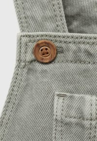 Siv denim material s teksturirano površino, z okroglo leseno gumbom in šivalnimi detajli blizu majhnega žepa na trak.