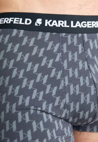 Sivi bokserice s ponavljajući svijetlosivi uzorak loga, s crnim elastičnim pojasom na kojem piše "KARL LAGERFELD" bijelim slovima.