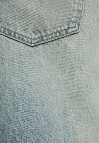 Tejido de mezclilla azul claro con un patrón de tejido diagonal visible y un primer plano de un bolsillo trasero con costuras naranjas.