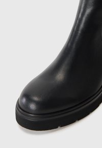 Botte chelsea en cuir noir avec un bout arrondi, une surface texturée et une semelle en caoutchouc épaisse comportant un léger motif de crampons.