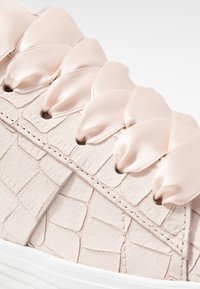 Różowe buty teksturowane z wzorem krokodylej skóry, z satynowymi sznurowadłami i białą gumową podeszwą. Zbliżenie na obszar sznurowania i materiał buta.