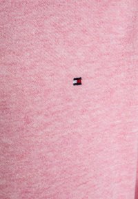 Różowa dzianina z małym prostokątnym logo, które w centralnej części ma czarne, białe i czerwone poziome paski.