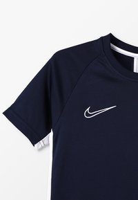 Marinblå kortärmad skjorta med vita detaljer och Nike-logotyp. Tillverkad av andningsbart material, med rund halsringning och en texturerad design.