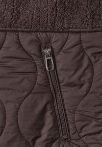 Close-up of brown quilted fabric with metal zipper and textured knit trim.