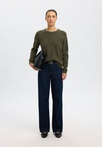 Olivgrüner Pullover, hoch taillierte dunkelblaue Jeans mit weitem Bein und schwarze Ledertasche. Einfaches Design, strukturierter Stoff. Schwarze Schuhe.
