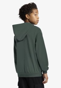 Žalia gobtuvu megztinė su lygiu tekstūra, elastinėmis rankogaliais ir apačia, turinti laisvą siluetą be matomų logotipų ar dekoro.