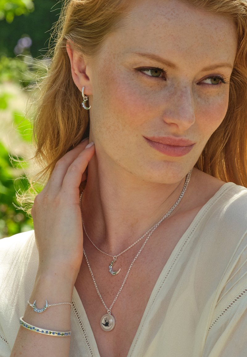 Joyas de plata que incluyen collares en capas con detalles de luna creciente y colgantes, aretes con acentos sutiles y una pulsera con incrustaciones coloridas.