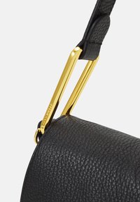 Sangle de sac en cuir noir texturé avec un clip en métal doré. La sangle présente un rembourrage en cuir lisse et le nom de la marque gravé sur le matériel.