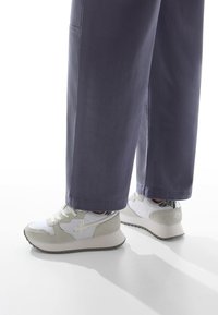 Bílé a šedé tenisky mají kombinaci hladkého a semišového povrchu, vroubkovanou podrážku a reflektivní stříbrný akcent na patě.