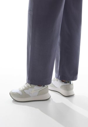White and grey sneakers feature a mix of smooth and suede textures, a ridged sole, and a reflective silver accent on the heel.