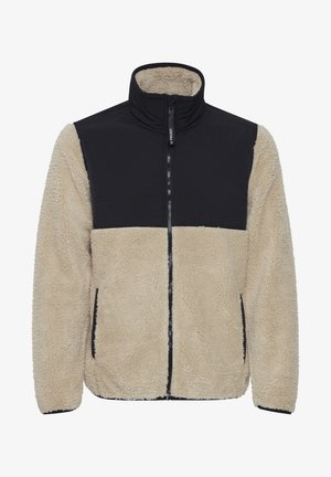 Beige fuzzy fleece jas met een zwart gewatteerd bovenstuk, hoge kraag, volledige ritssluiting aan de voorkant en zijzakken. Geweven stofdetails zijn zichtbaar.