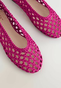 Chaussures plates tissées rose vif avec un motif en treillis ouvert et des semelles intérieures beige, vues de dessus sur une surface claire.