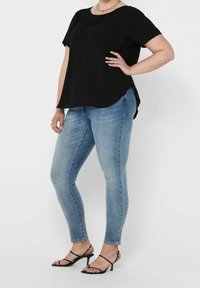 Top noir à manches courtes avec un ourlet courbe, associé à un jean skinny bleu clair et des sandales noires à lanières, mettant en avant un look décontracté.