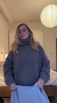 Jeune femme aux yeux fermés tenant une couverture pliée dans une chambre avec des murs beige, un lit et une lampe de plafond ronde.