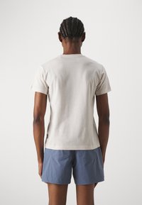 Lichtbeige katoenen t-shirt met korte mouwen, een ronde halslijn en een lichte stretch. Draagt met blauwe shorts, met twee achterzakken.