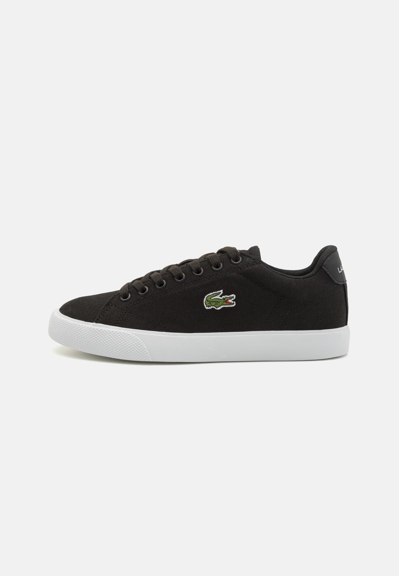 Baskets basses noires avec semelle blanche, design à lacets et logo crocodile vert sur le côté.