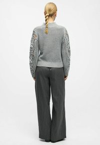 Pull en tricot gris avec des manches ajourées. Pantalon à taille haute, à jambes larges et rayé. Texture lisse, design décontracté avec une coupe ample.