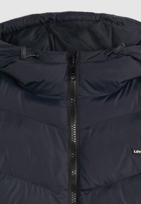 Casaco acolchoado azul-marinho com capuz, apresentando um fecho zip preto central e um pequeno logótipo da Levi's no canto inferior esquerdo. Textura lisa e acolchoada.