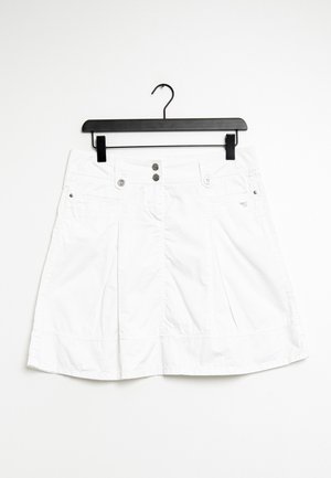 Jupe plissée blanche avec deux poches avant, boutons en métal à la taille, et une texture lisse semblable à du coton. Suspendue à un cintre en plastique noir.