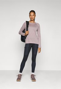 Helles rosa Langarmshirt, schwarzer Rucksack, dunkelblaue Leggings mit Taschen und braune Sportschuhe mit rosa Akzenten. Einfaches modernes Design.