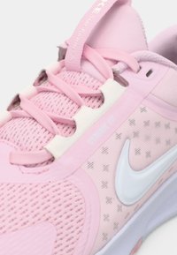 Gros plan sur une chaussure de course rose avec le logo Nike blanc, des lacets roses et le texte "Dynamic Fit" sur le panneau latéral.