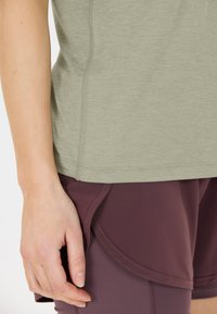 Top de color verde oliva y mangas cortas combinado con pantalones cortos deportivos color marrón. La parte superior tiene una textura suave y un dobladillo recto; los pantalones cortos presentan detalles de diseño en capas.