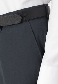 Sötétkék nadrág sima textúrával, fekete bőrbelt tartalmaz, és a jobb oldalon egy hófehér ingujj látható.