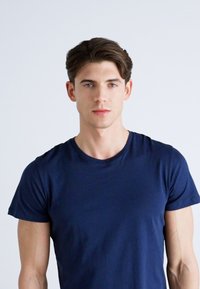 Camiseta de algodón azul marino de manga corta, con cuello redondo y un diseño ajustado, llevada por un modelo masculino sobre un fondo neutro.